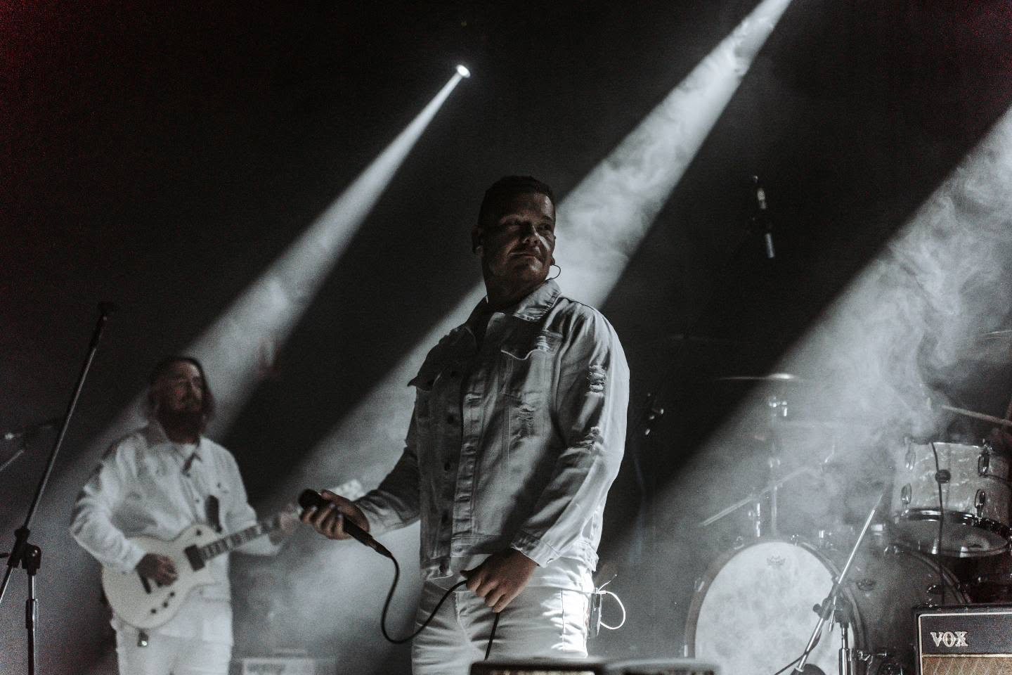 New Anomaly frontman on stage lit by dramatic spotlights through haze, black and white